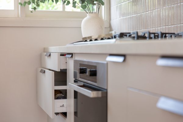 Light grey cabinetry with different size drawers including cutlery and pot drawer open to display depth next to stainless steel oven