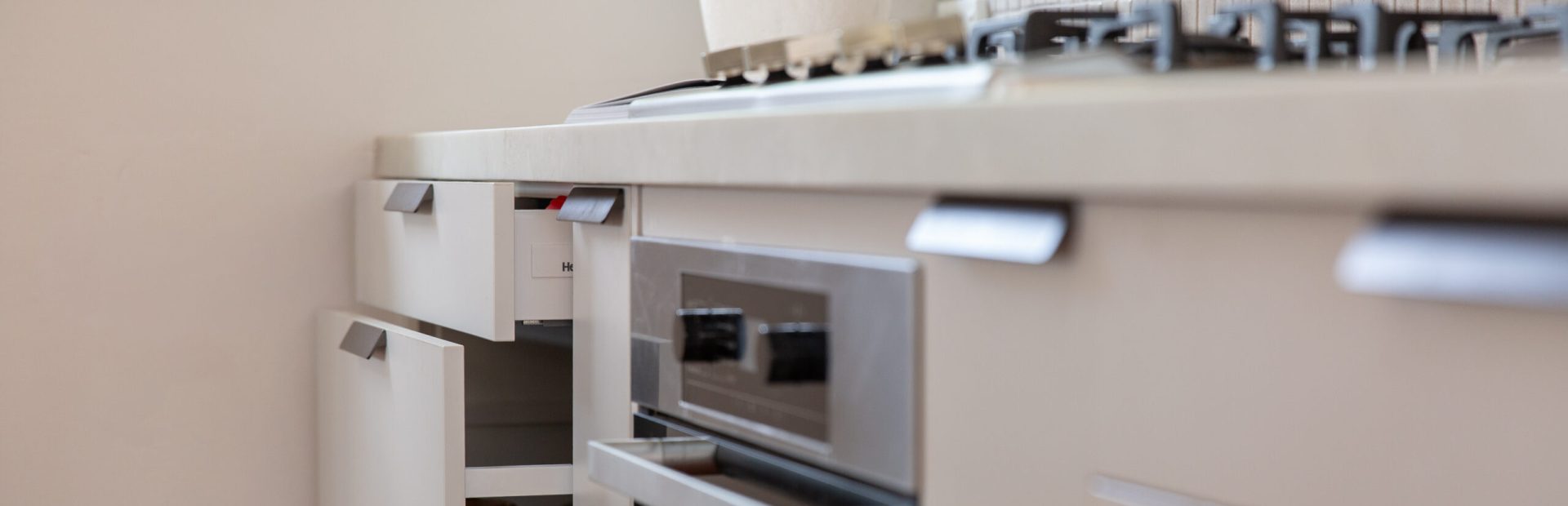 Light grey cabinetry with different size drawers including cutlery and pot drawer open to display depth next to stainless steel oven