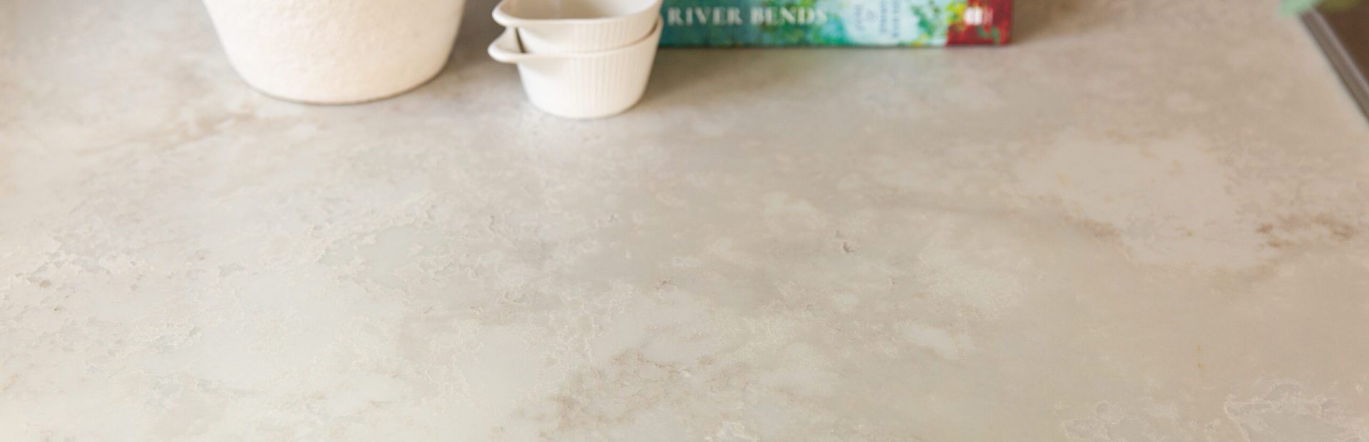 Marbled style stone benchtop called Jade Sky with vase, receipe book and three small white containers