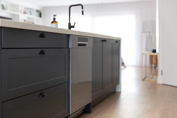 Dark grey shaker style kitchen in a row featuring drawers and cupboards and a stainless steel dishwasher with black sink and tap above