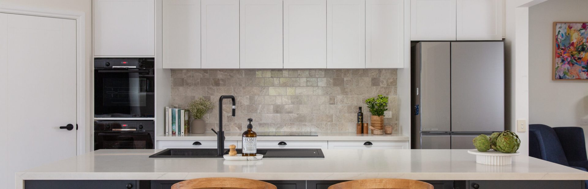 Galley style shaker kitchen featuring white and dark grey cabinetry with black wall oven tower and stainless steel fridge
