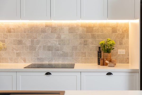 White shaker style cabinetry in kitchen with induction cooktop and grey tiled splashback with vase and flowers on benchtop