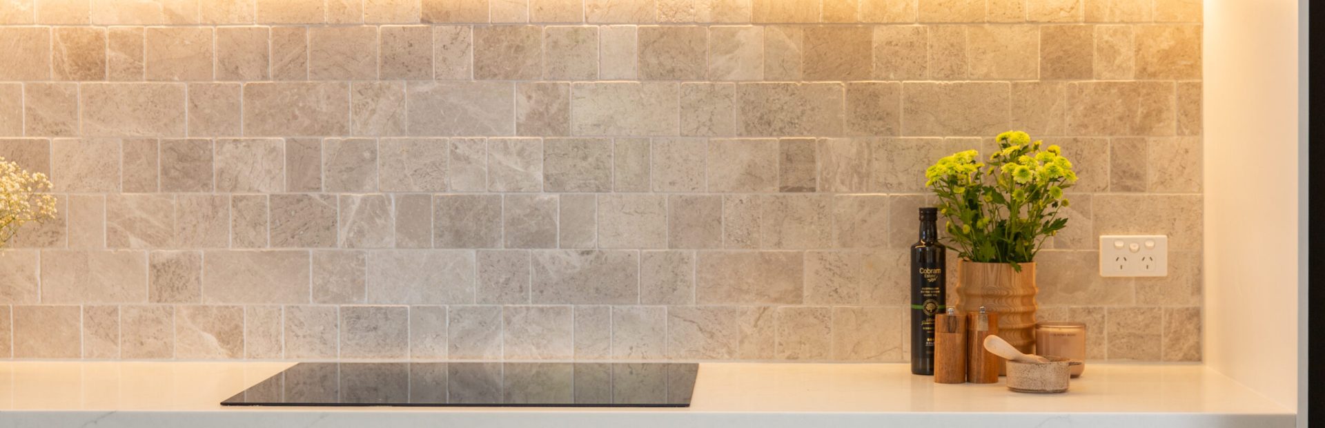 White shaker style cabinetry in kitchen with induction cooktop and grey tiled splashback with vase and flowers on benchtop