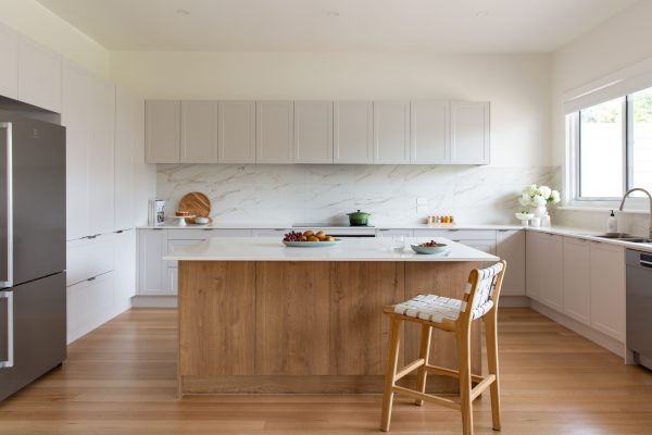 White kitchen cabinetry displaying pantry cabinet with one door open and pantry items inside, cake on cake stand with books on stone benchtop