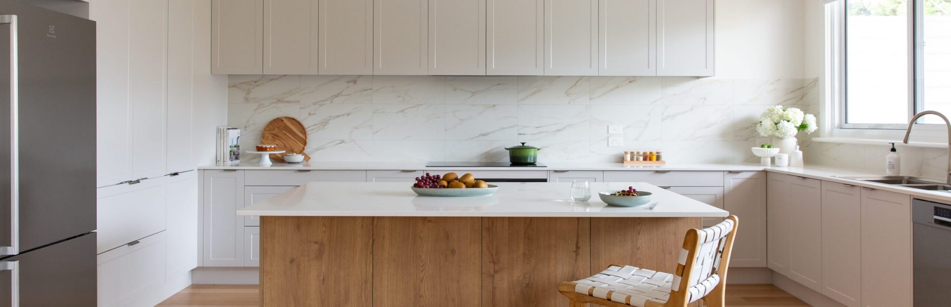 White kitchen cabinetry displaying pantry cabinet with one door open and pantry items inside, cake on cake stand with books on stone benchtop