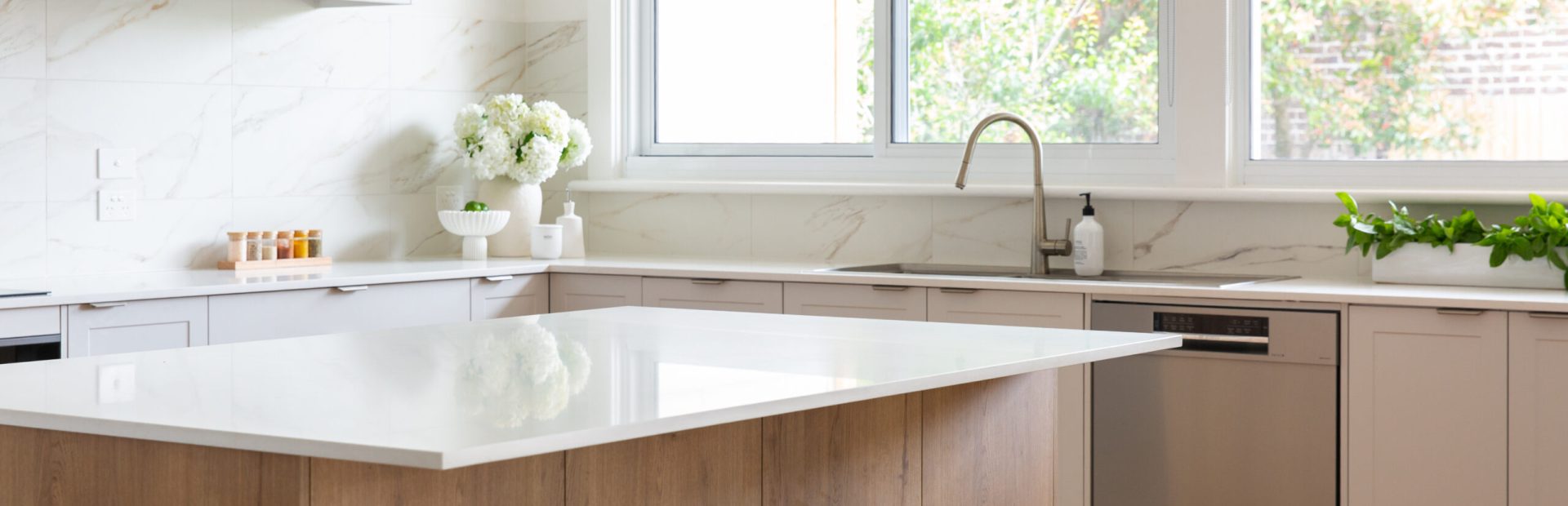 Kitchen displaying large island bench in the centre with overhang in white stone and underneath oak timber cabinetry with two green benchstools