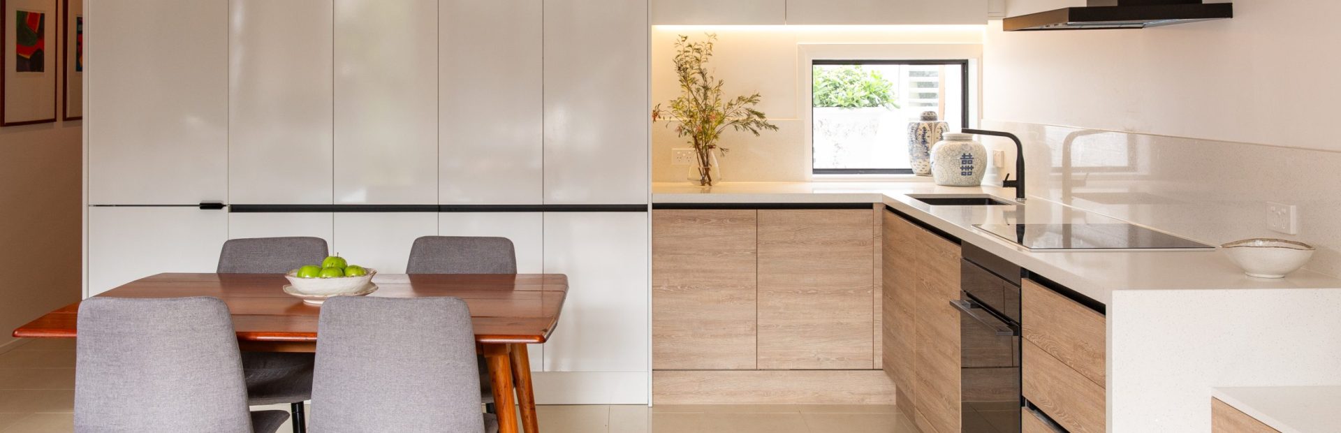 U shaped kitchen with white cabinetry to the ceiling and rural oak timber laminate underbench cabinetry with black rangehood and dining table