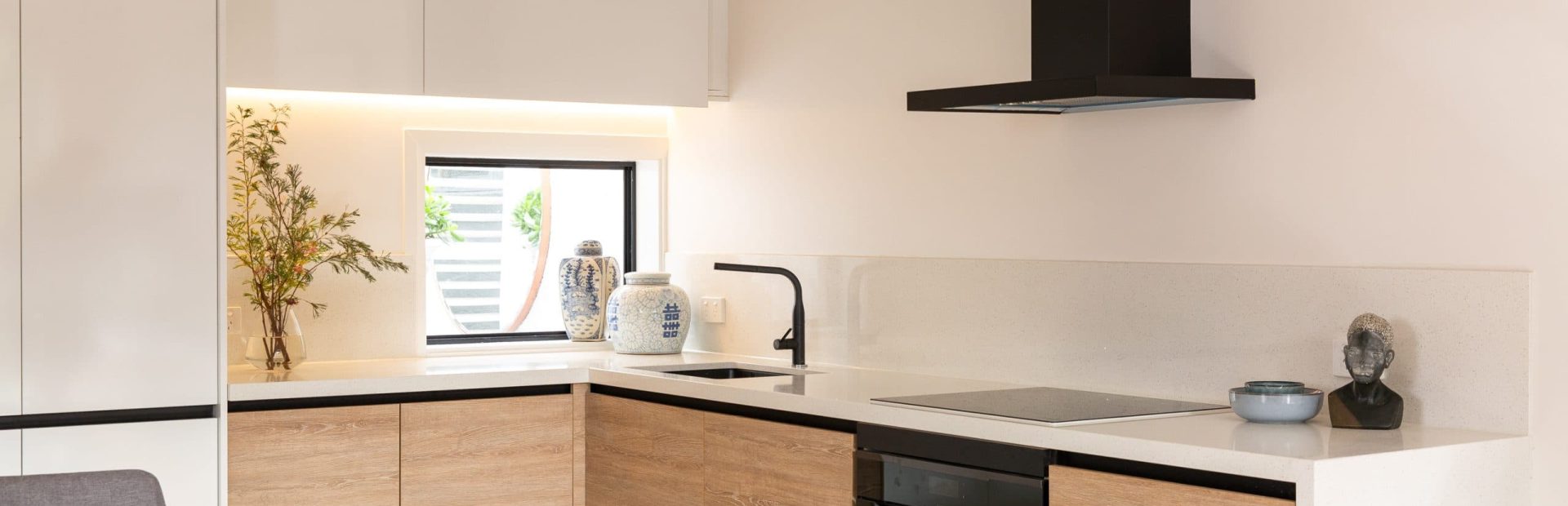 u shaped kitchen with timber laminate cabinetry and white benchtops with black rangehood and black oven