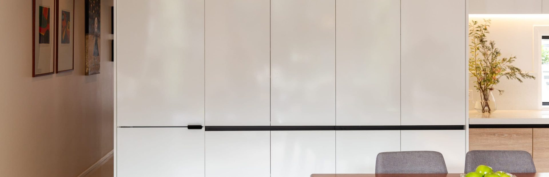 Bank of white cabinetry doors to the ceiling and timber dining table with grey chairs