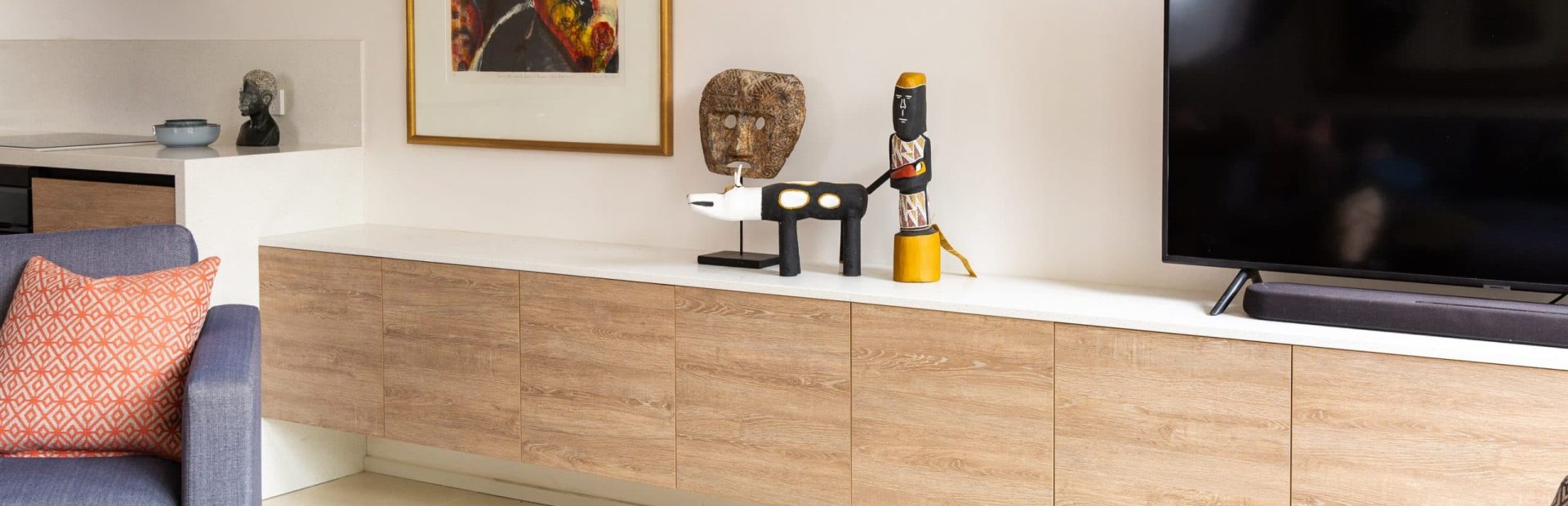 Living room cabinetry featuring oak timber and white benchtops that a black TV sits on top