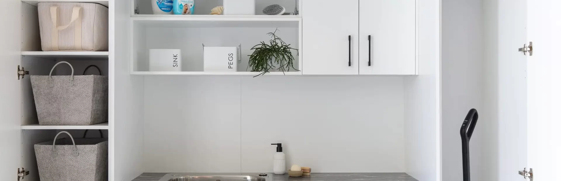 galley style laundry displaying open shelves with white cabinetry and black benchtop displaying cleaning products