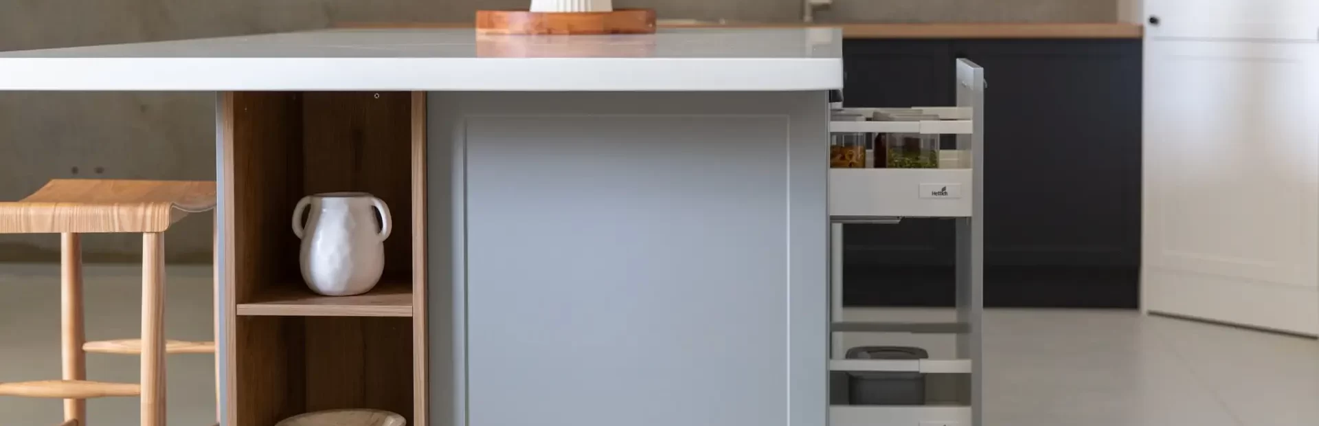 Island bench in grey cabinetry with timber stool and timber open shelf displaying vases