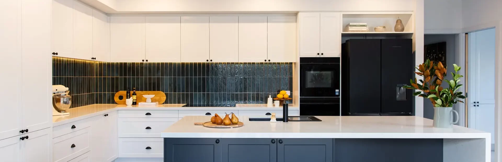 U shaped kitchen with white and grey shaker style cabinetry with large standalone island bench and green tiled splashback