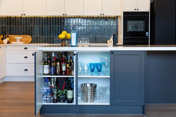Grey shaker style cabinetry in an island bench in this kitchen with bar bottles, glasses and ice bucket ready to make an alcoholic drink