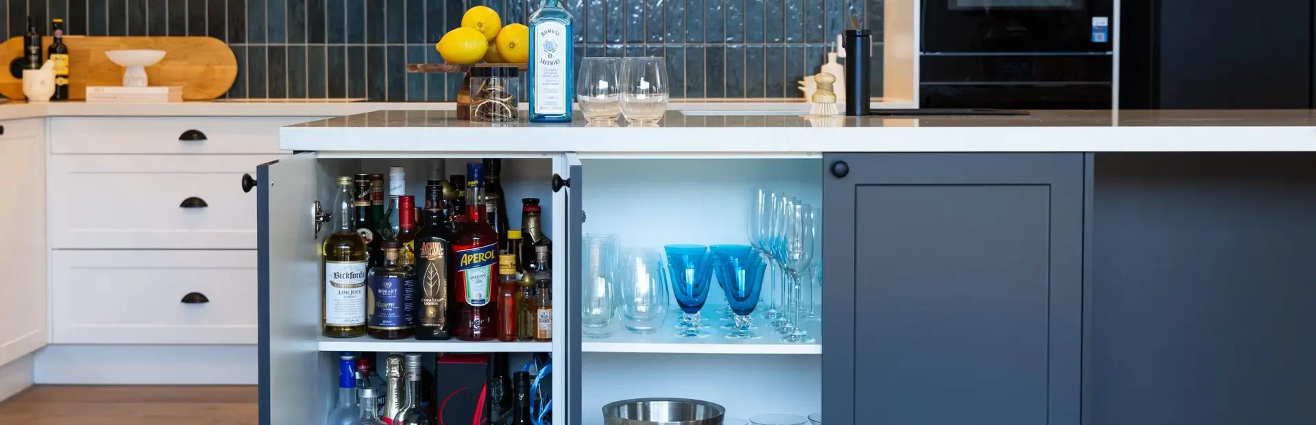 Grey shaker style cabinetry in an island bench in this kitchen with bar bottles, glasses and ice bucket ready to make an alcoholic drink