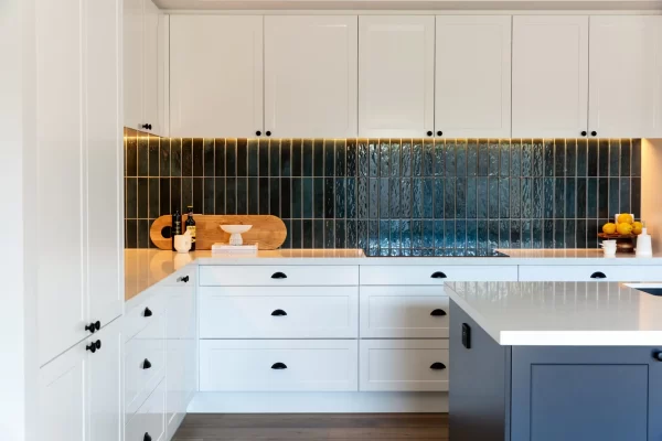White shaker style kitchen cabinetry with black handles and green tiled splashback