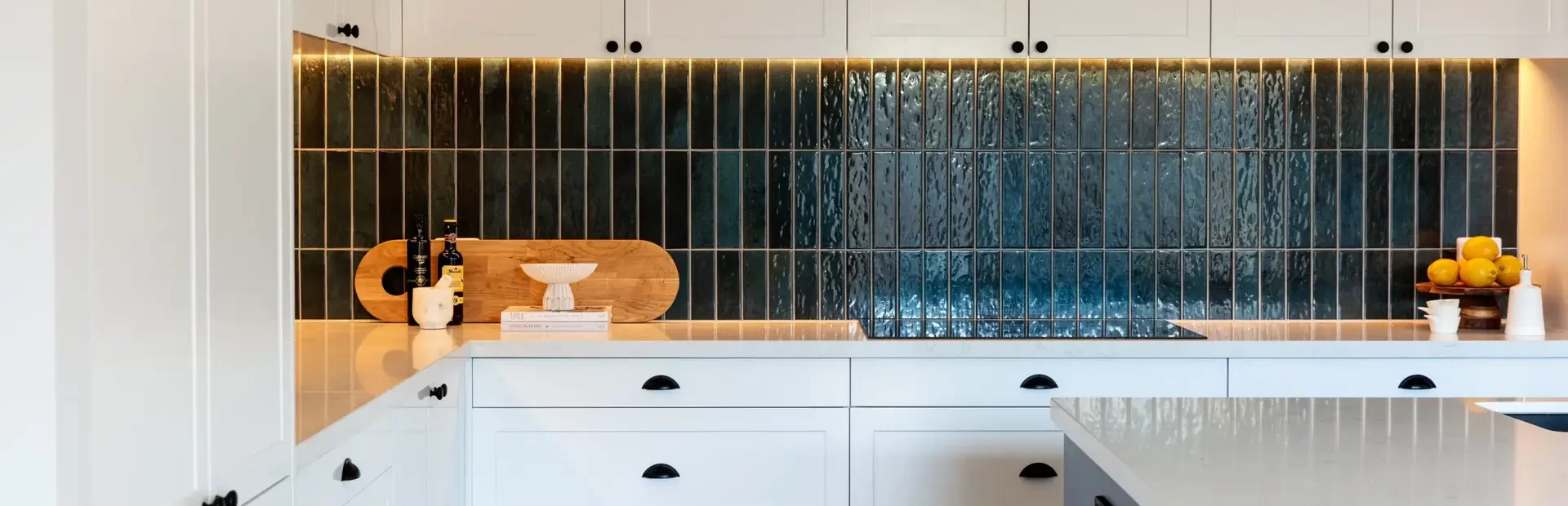 White shaker style kitchen cabinetry with black handles and green tiled splashback