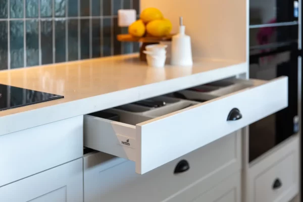 White shaker kitchen cabinet displaying deep narrow drawer and white stone benchtops with condiments and lemons for styling