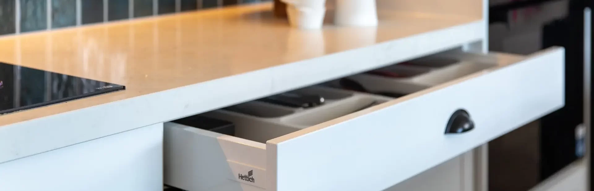 White shaker kitchen cabinet displaying deep narrow drawer and white stone benchtops with condiments and lemons for styling