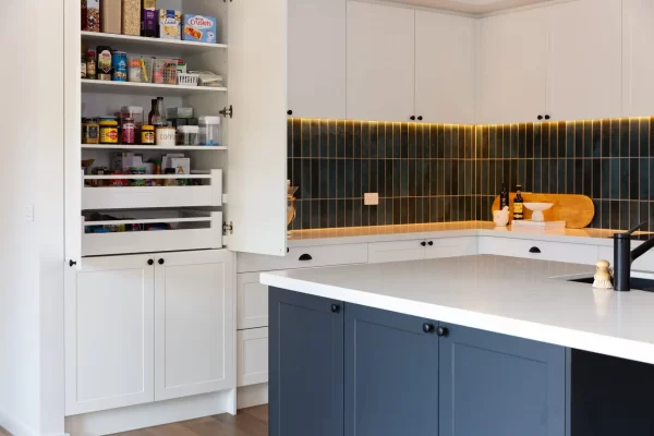 White and grey kitchen cabinetry in u shaped kitchen with green splashback tiles and pull out pantry drawers inside