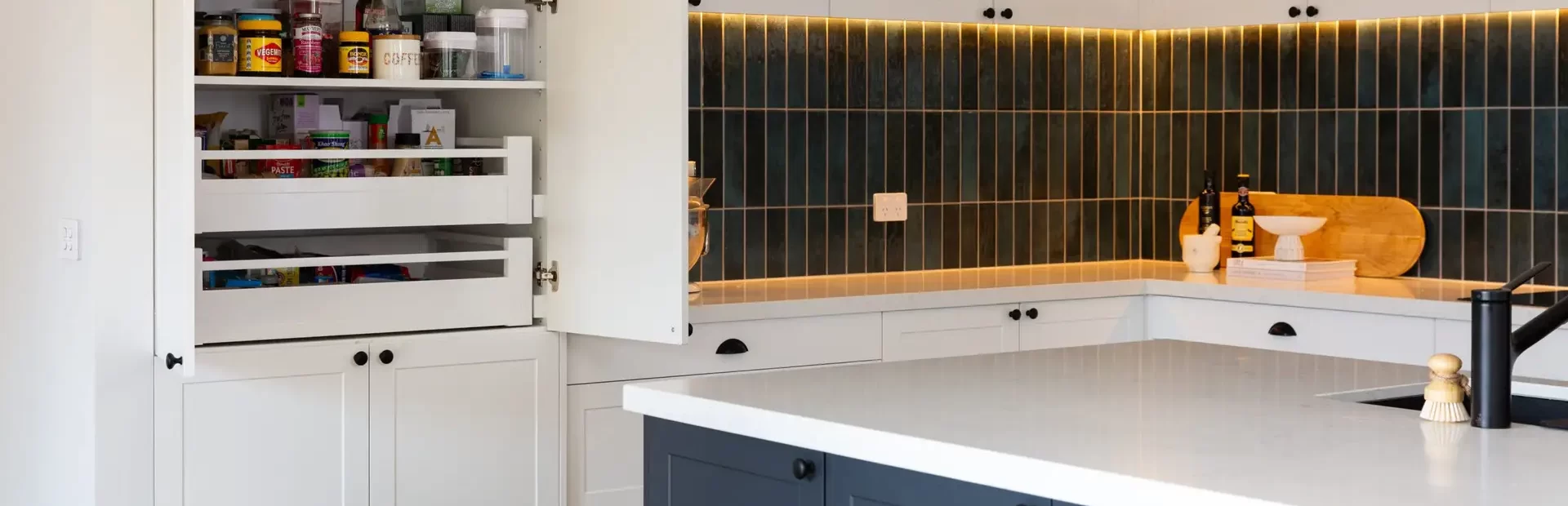 White and grey kitchen cabinetry in u shaped kitchen with green splashback tiles and pull out pantry drawers inside