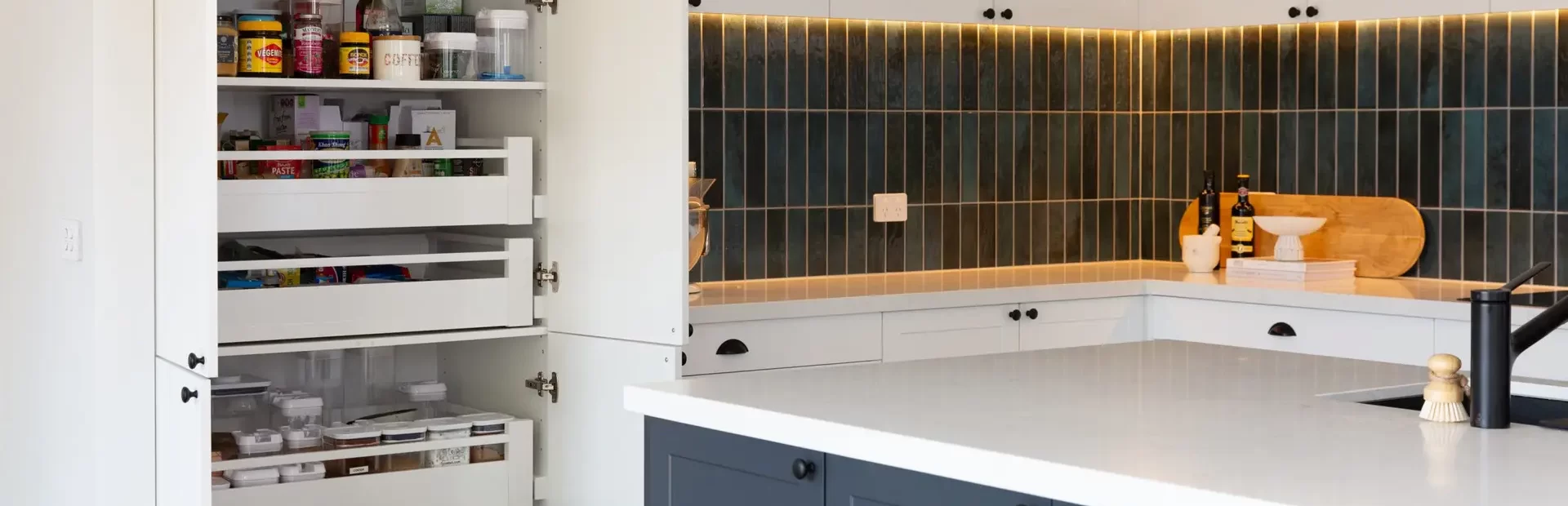 Kitchen pantry with pull out shelves for easy storage and reach including green tiled splashback