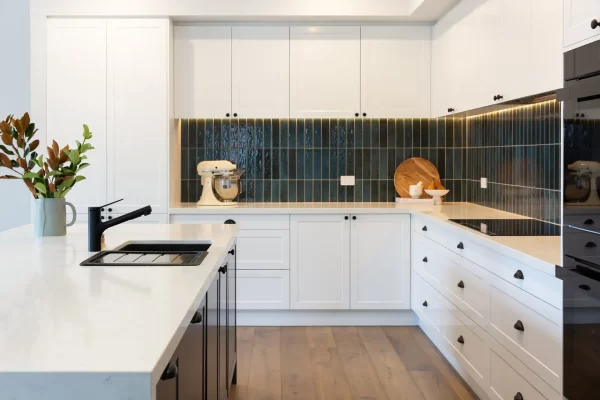 U shaped white and grey shaker style kitchen with white stone benchtops and green splashback tiling with styling items of boards and mix master