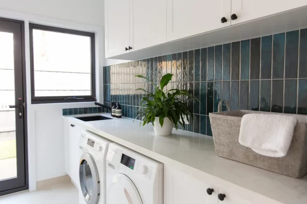White kitchen cabinetry in galley style laundry with green splashback tiles leading to outside