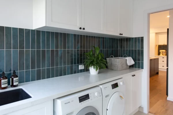 Galley style kitchen with white shaker style cabinetry and white stone benchtops with green tiled splashback