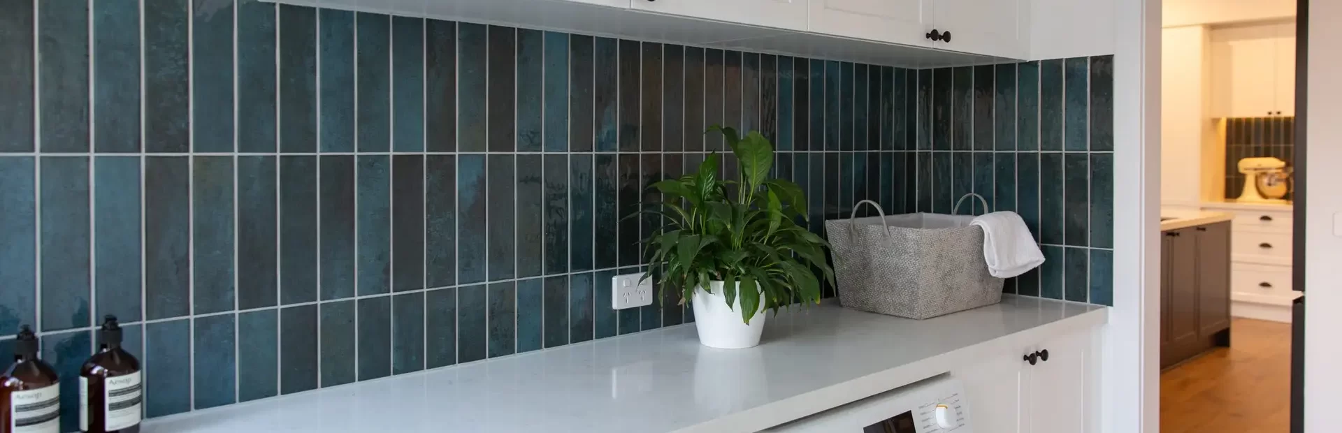 Galley style kitchen with white shaker style cabinetry and white stone benchtops with green tiled splashback
