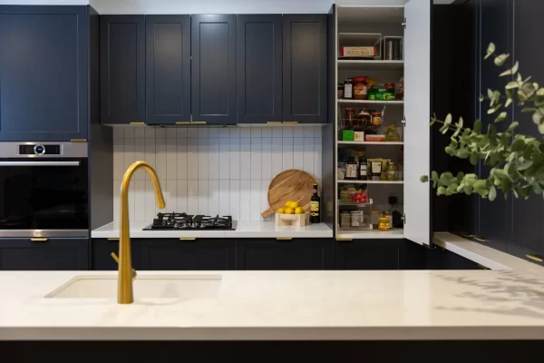 Corner pantry in a dark shaker kitchen with a white benchtop and brass tap