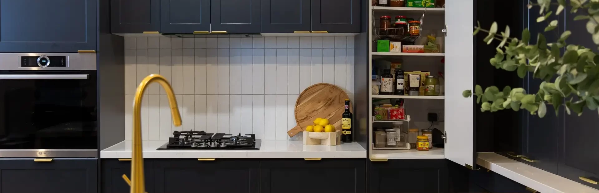 Corner pantry in a dark shaker kitchen with a white benchtop and brass tap