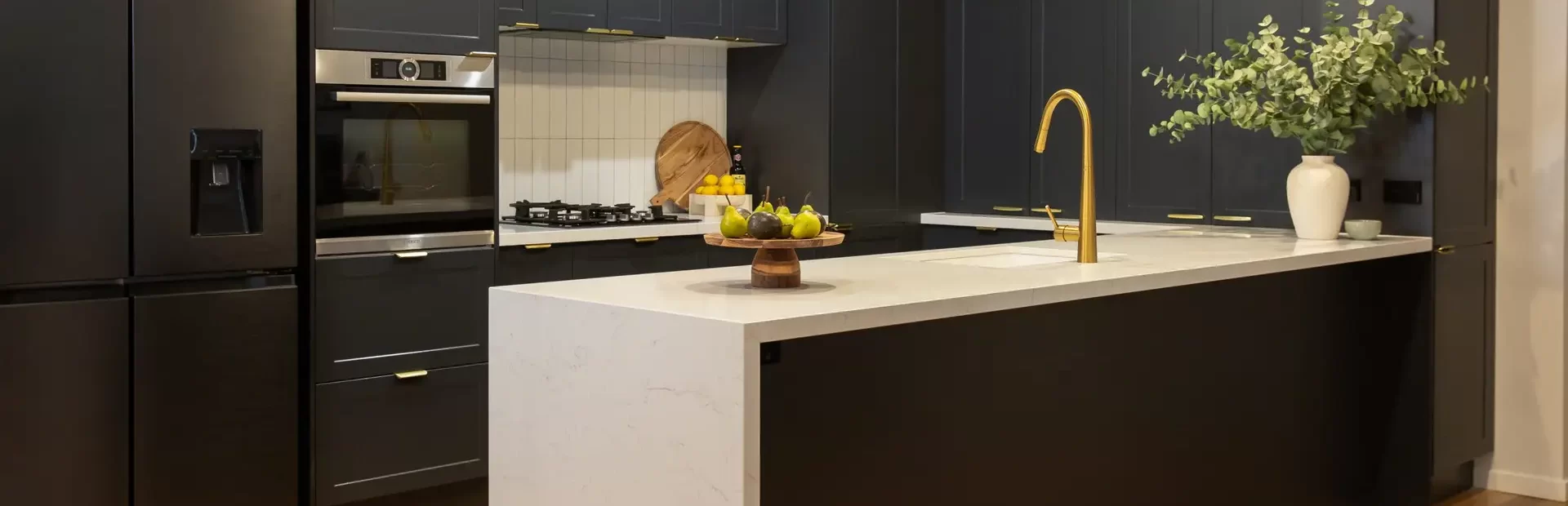 U shaped dark black cabinetry with white benchtops and waterfall ends on island bench