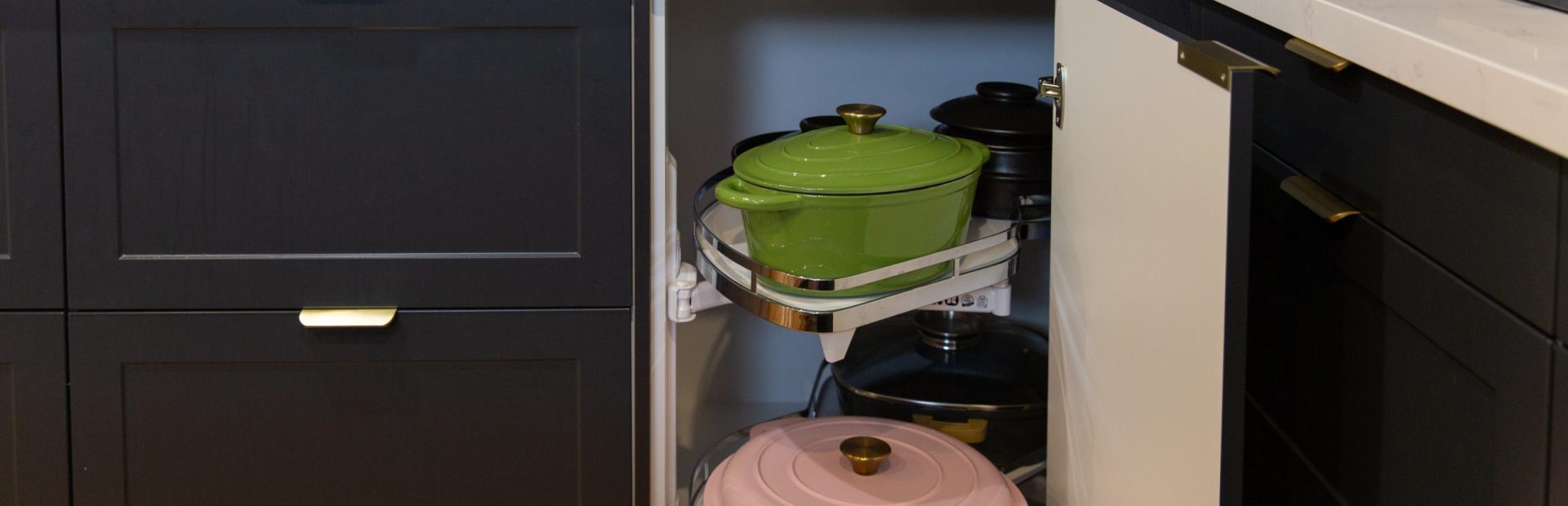 Pull out corner le mans kitchen cabinet displaying a pink and green le creuset pots