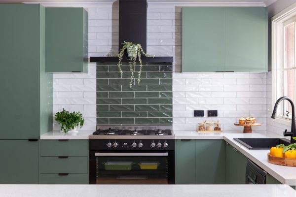 U shaped kitchen featuring sage green cabinetry with white stone benchtops and white and green tiled splashback