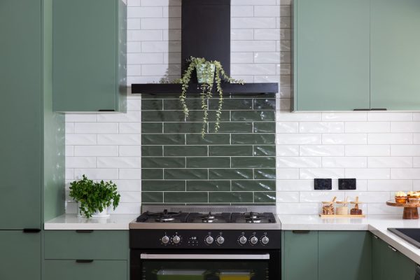 Green kitchen cabinetry with black pull handles and white and green subway tiles