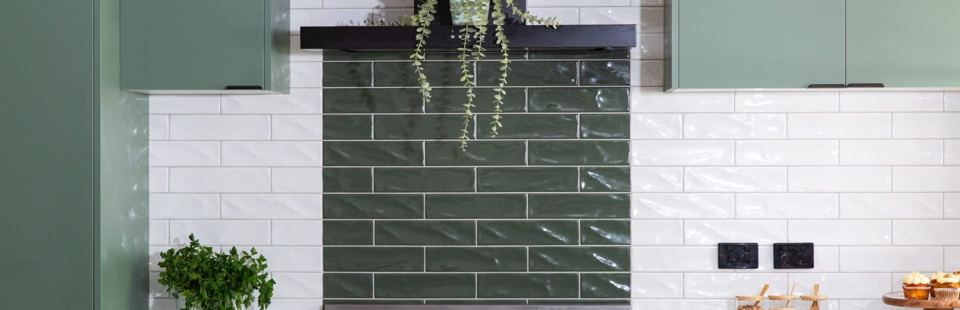 Green kitchen cabinetry with black pull handles and white and green subway tiles