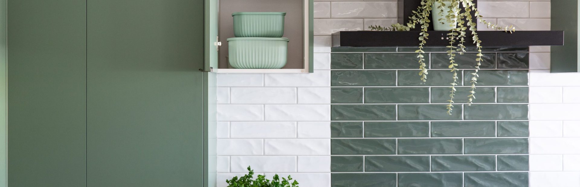 Dark green cabinetry featuring pantry and white and green subway tiles