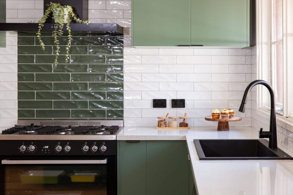 U shaped kitchen with green matt cabinetry and white stone benchtops with black sink and handles
