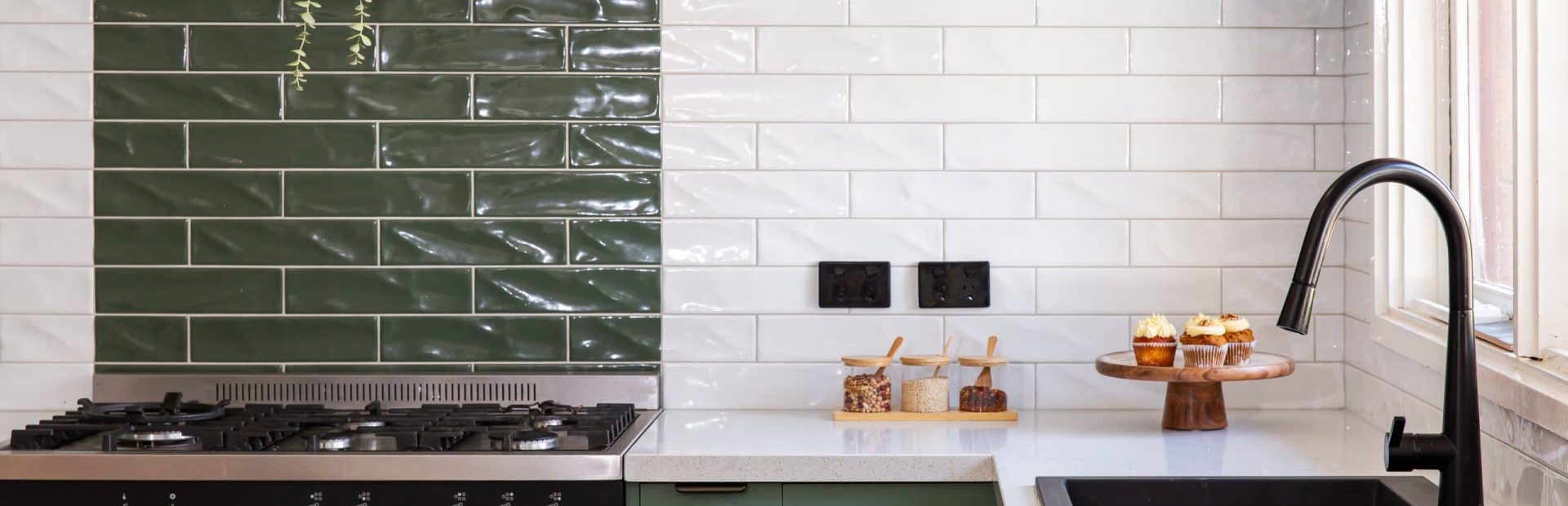 U shaped kitchen with green matt cabinetry and white stone benchtops with black sink and handles