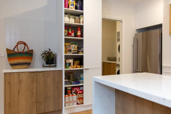 White and oak timber kitchen displaying a tall pantry with cooking essentials and neighbouring laundry