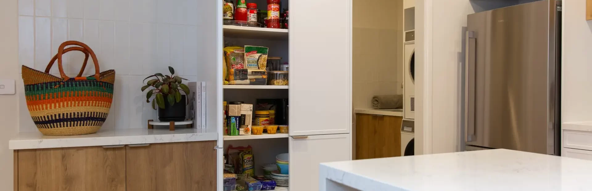 White and oak timber kitchen displaying a tall pantry with cooking essentials and neighbouring laundry