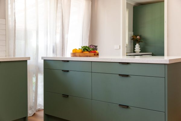 Large green bank of cabinetry drawers for pots and pans and white stone benchtops
