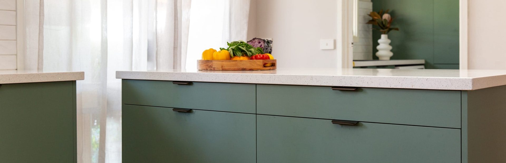 Large green bank of cabinetry drawers for pots and pans and white stone benchtops