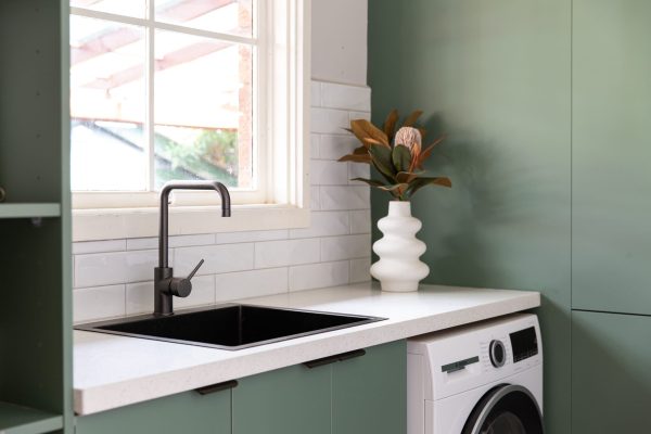 Green laundry cabinetry with white stone benchtops