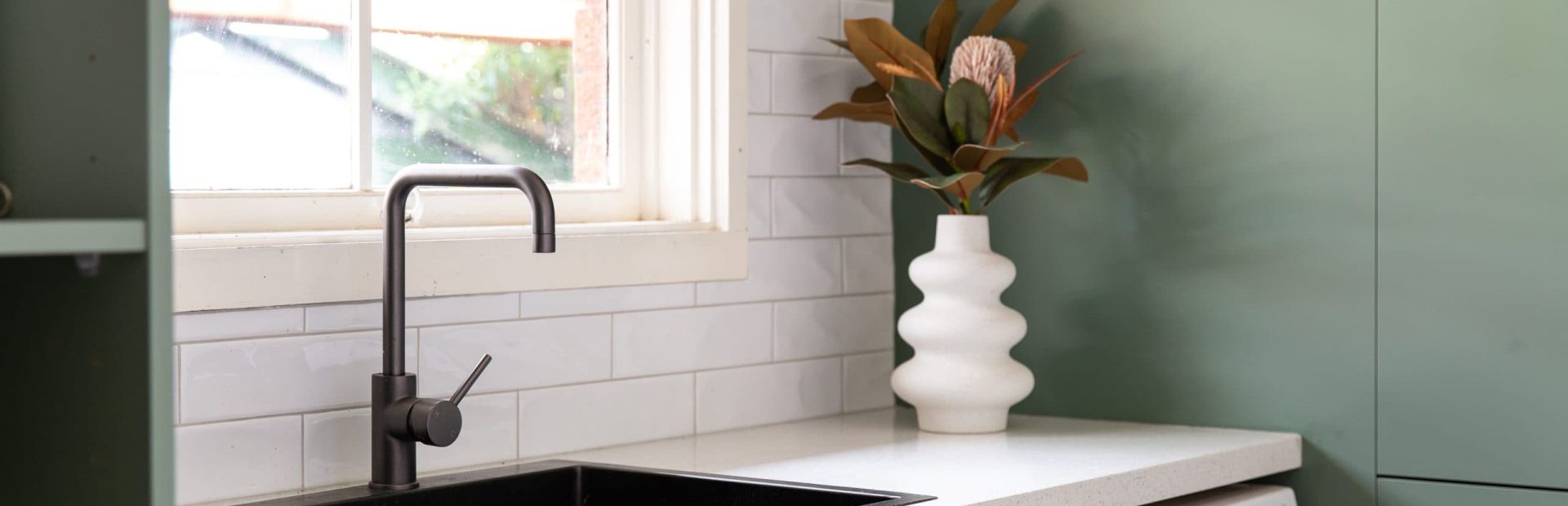 Green laundry cabinetry with white stone benchtops