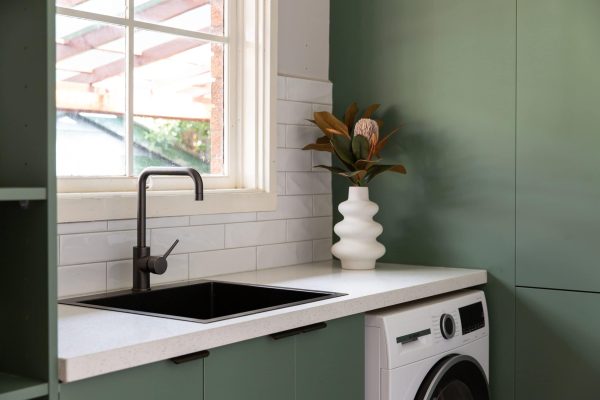 Sage green laundry cabinetry with black pull handles and white stone benchtops