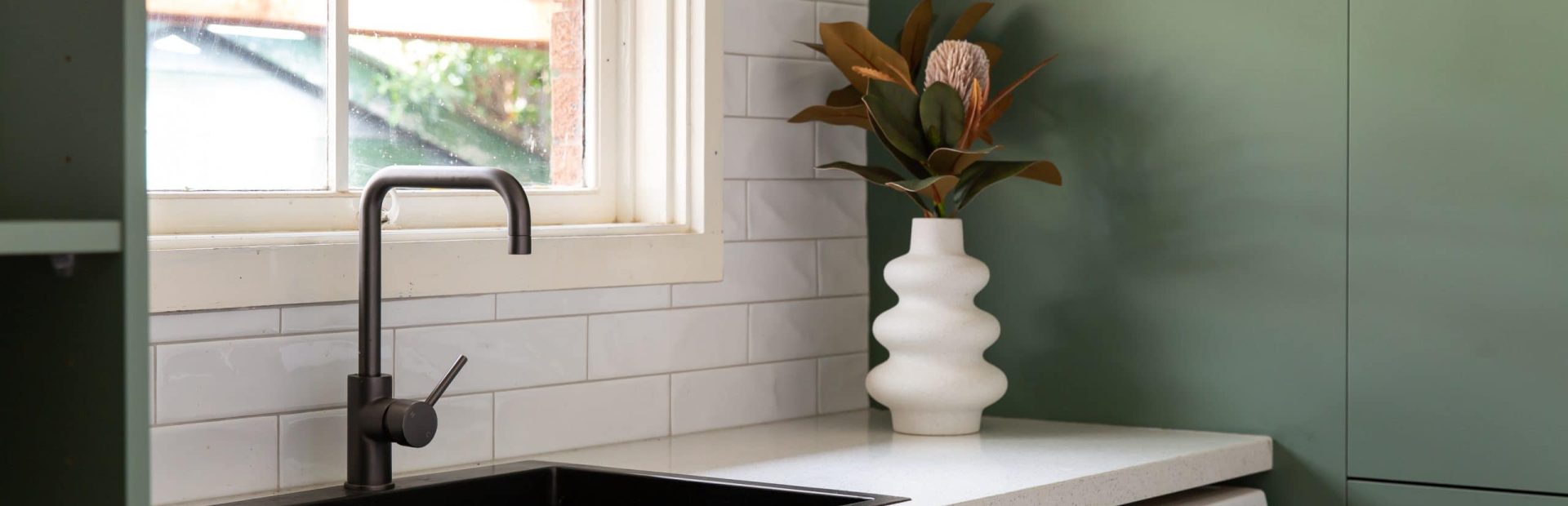 Sage green laundry cabinetry with black pull handles and white stone benchtops