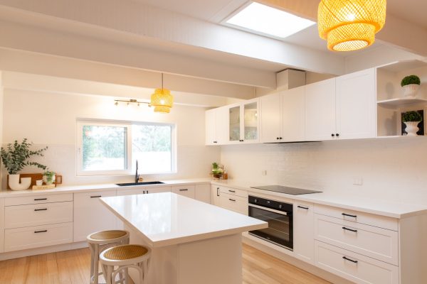 Shaker white style kitchen featuring black oven and glass cabinetry with large central island bench with timber stools