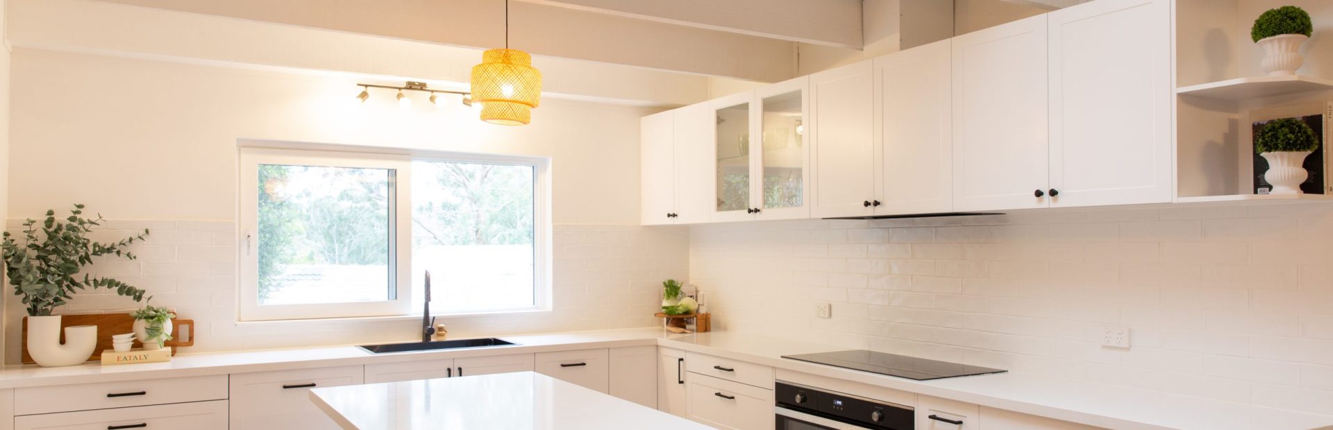 Shaker white style kitchen featuring black oven and glass cabinetry with large central island bench with timber stools